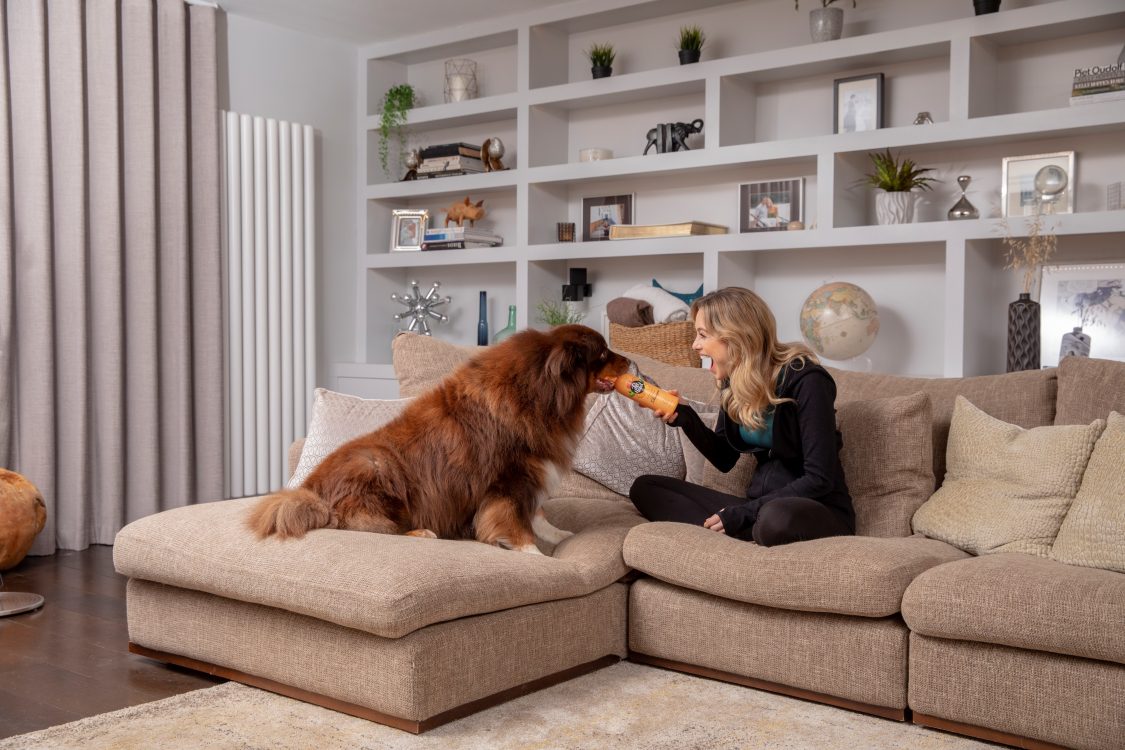 Woman laughing and playing with her collie who is nibbling on Ditch The Dirt shampoo bottle