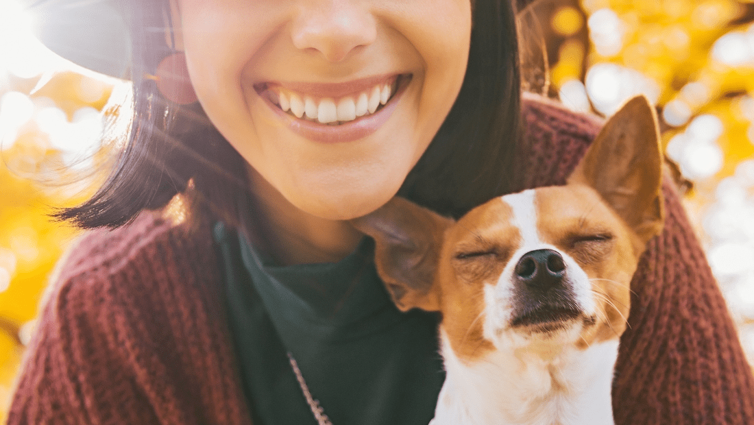 A dog smiling with a woman by some trees