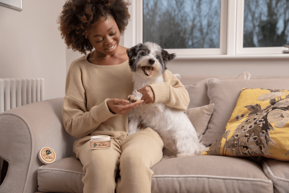 Image of woman holding small god on couch, enjoying using paw butter