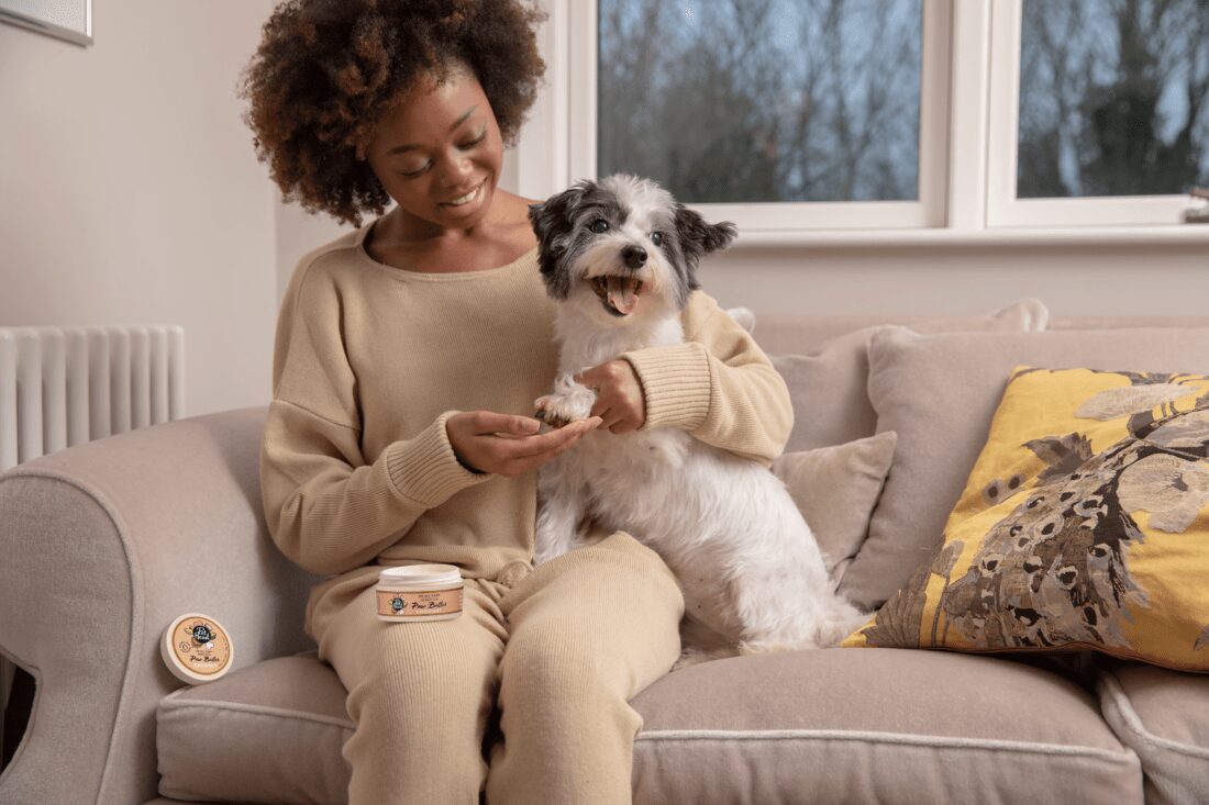 Image of woman holding small god on couch, enjoying using paw butter